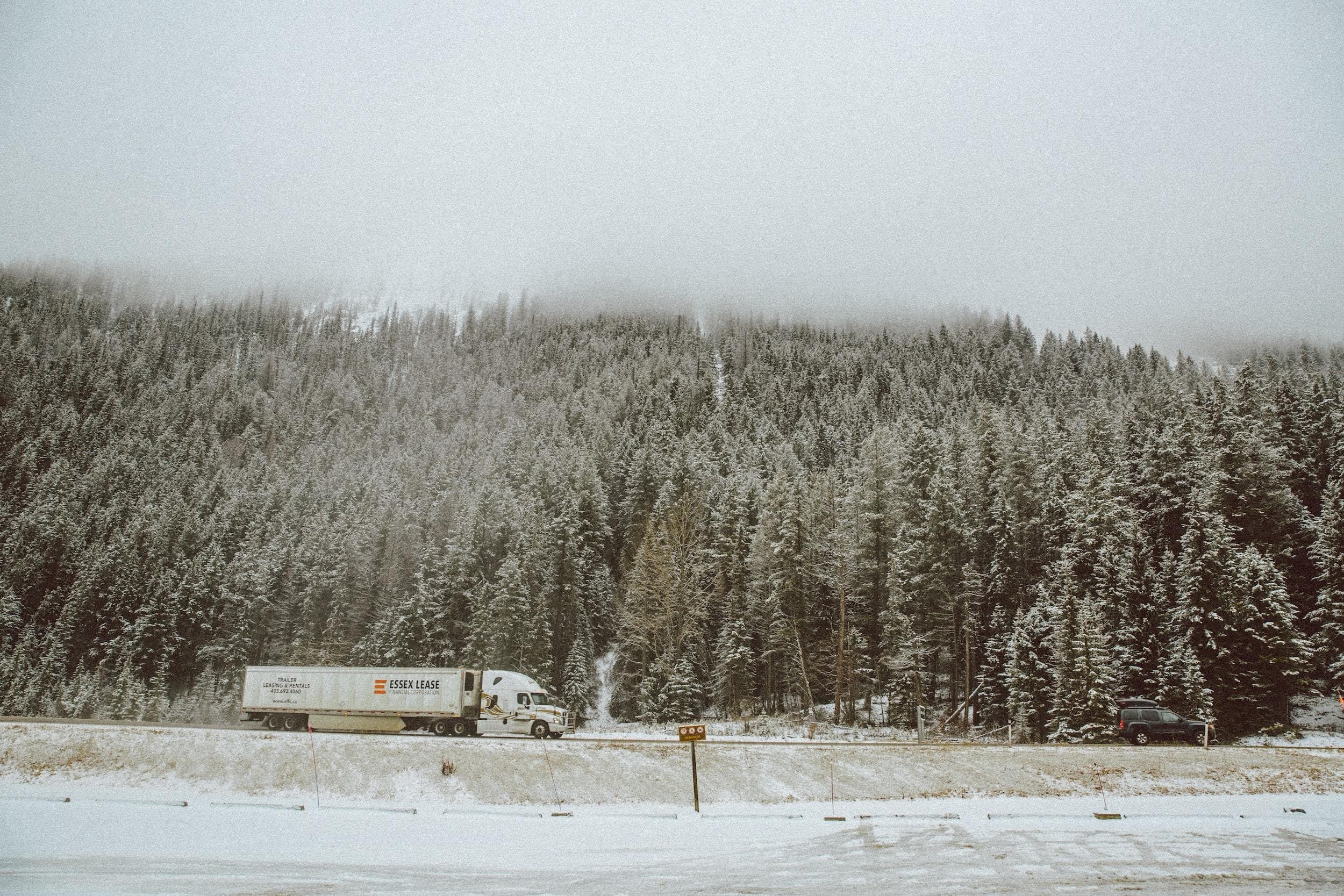 Truck on a road in the snow with a forest behind it
